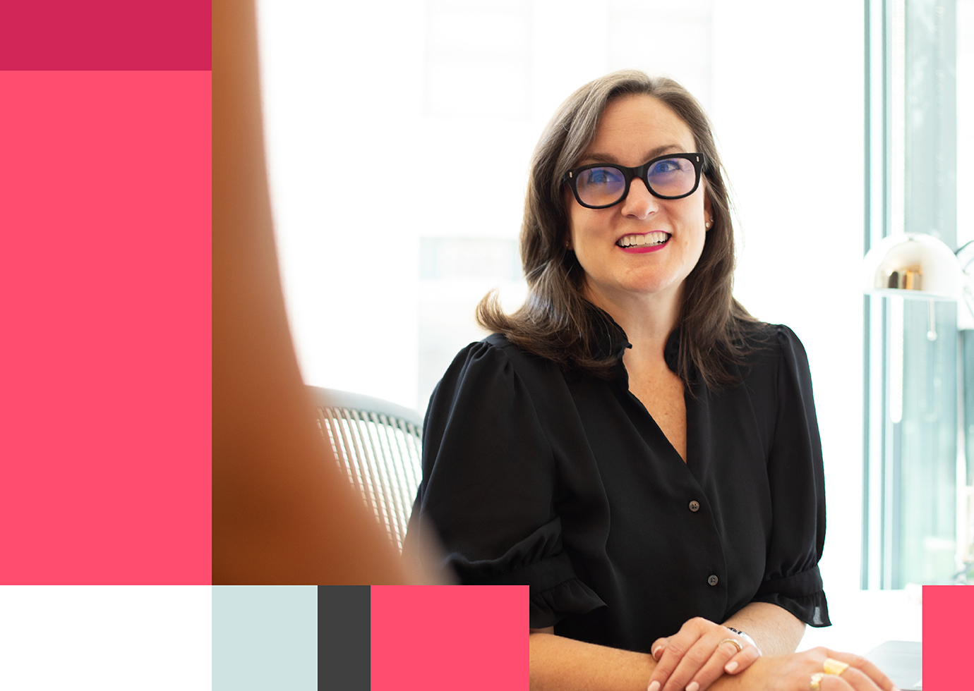 Thinkso founder Elizabeth Amorose sits at a desk, looking up and smiling towards someone out of frame.