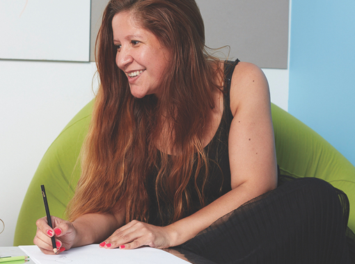 A woman sitting in a green chair smiles and takes notes.