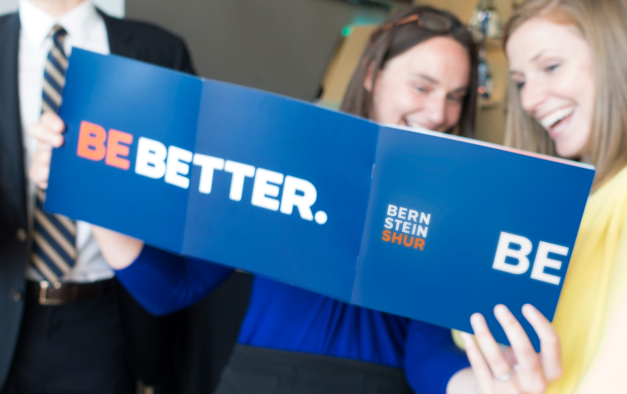 Two employees holding and looking at an opened Bernstein Shur brand spirit booklet with the title "Be better."