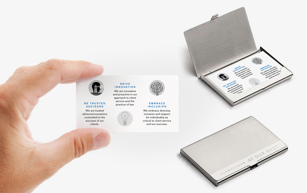 A hand holding an illustrated Cadwaleder "At our best" promotional card with two sets of the cards in cases in the background