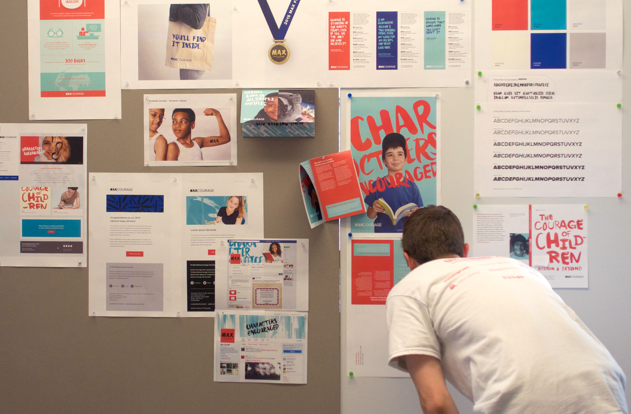 A person leans into to look at designs tacked to the wall for the 2015 Give A Brand design sprint.