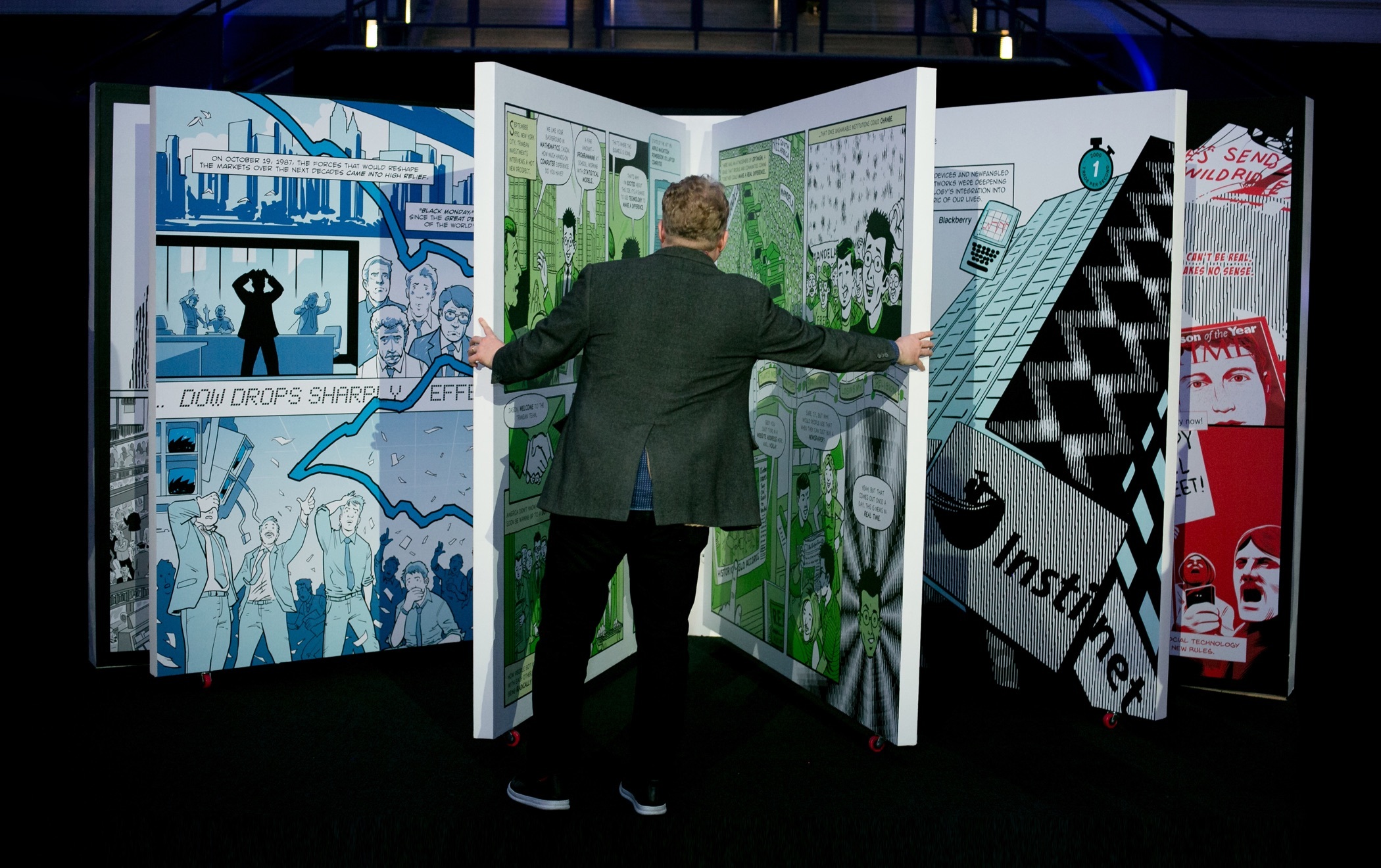 A rear view of a person opening the pages of a 7 foot tall version of Instinet's Fintech at Fifty graphic novel.