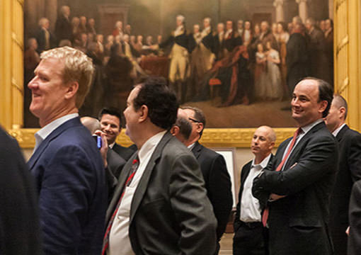 A group of 2014 KCG Uncon client event attendees in front of a painting of the signing of the Declaration of Independence.