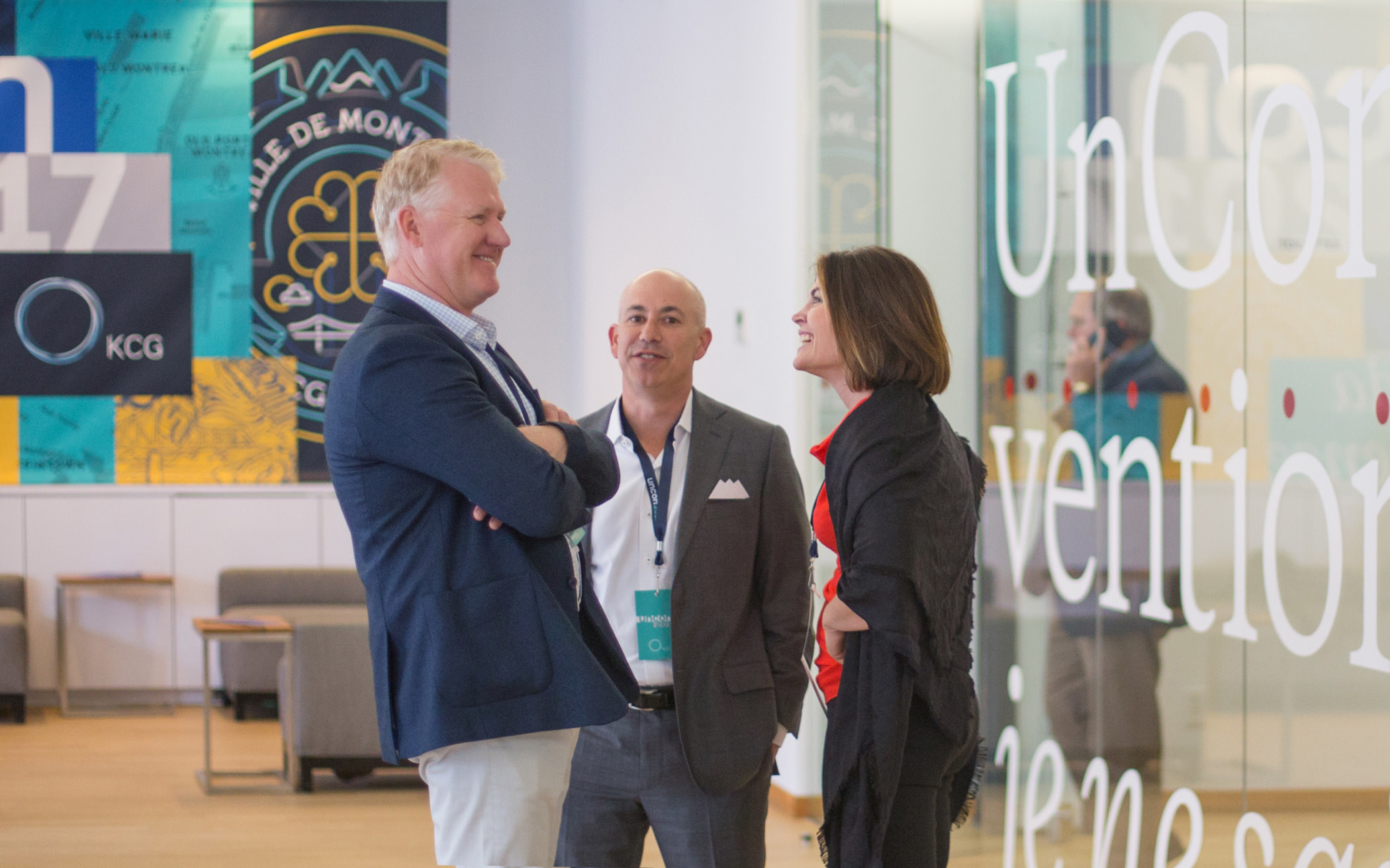 Three attendees speaking in an open space in front of colorful illustrated signs during the KCG annual "Uncon" client event.