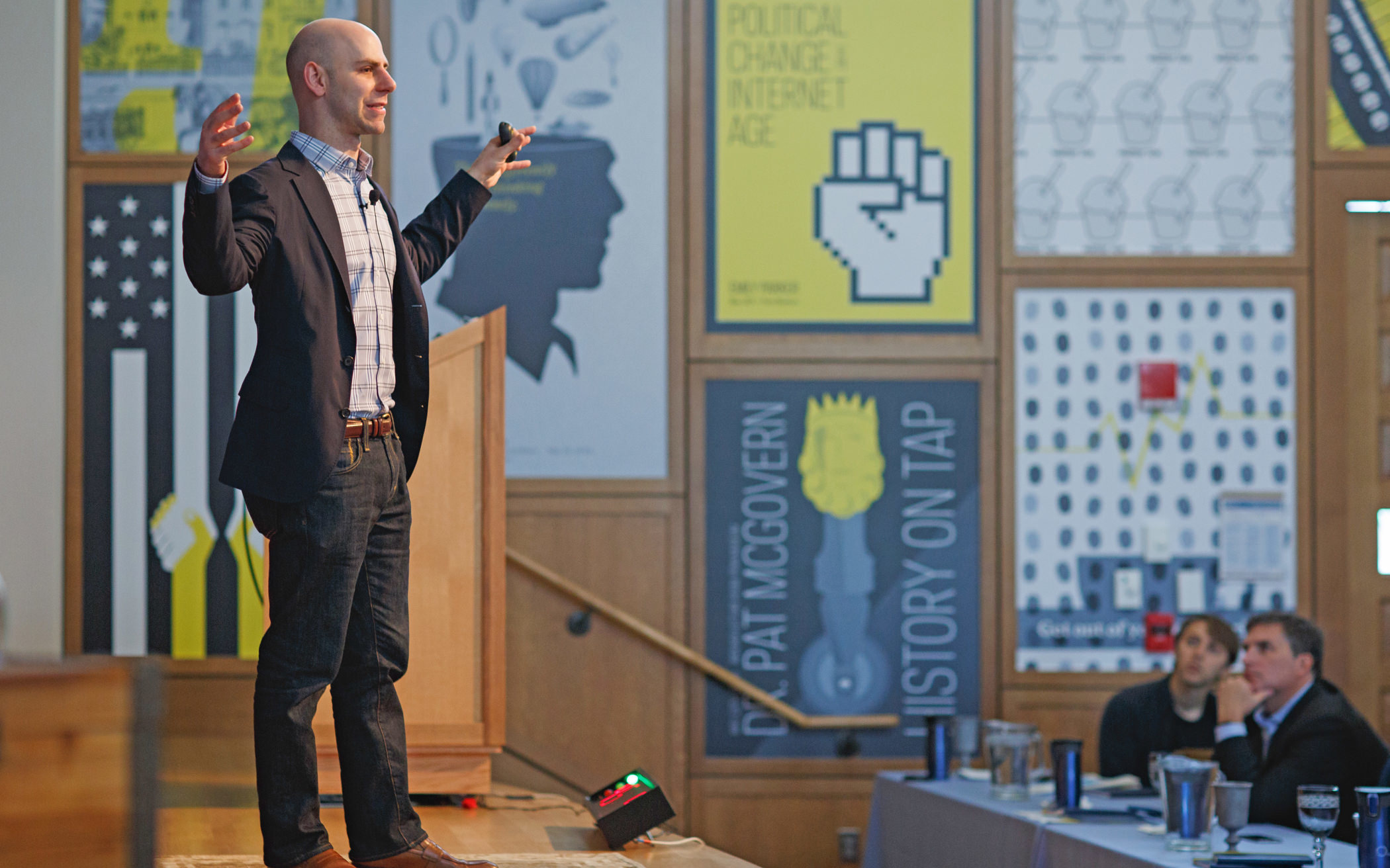 Standing profile view of male presenter with his hands aloft in a large room speaking at the 2014 KCG "Uncon" client event.