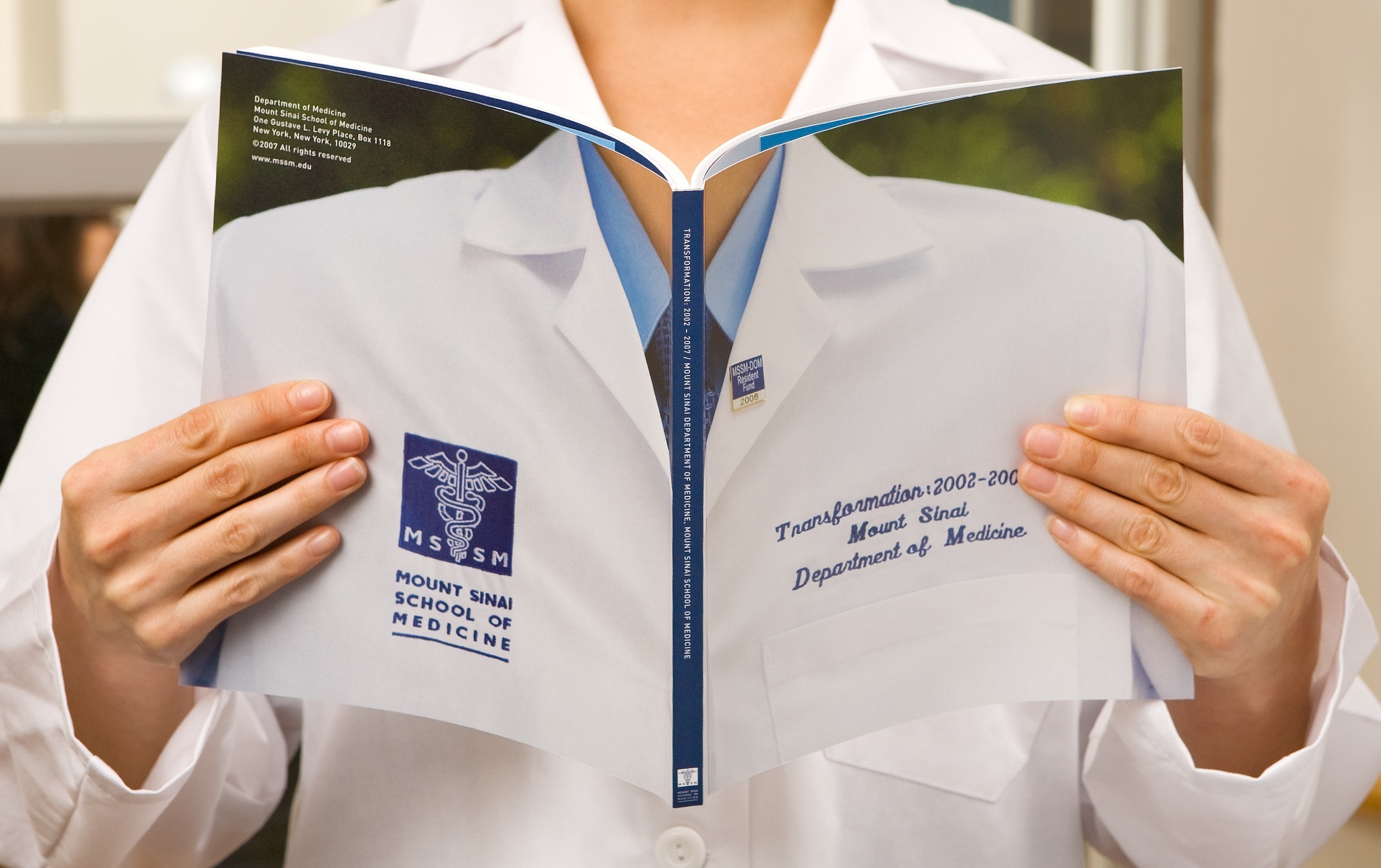 Hands holding open a Mount Sinai School of Medicine yearbook with an image of lab coat spread across the front and back cover.