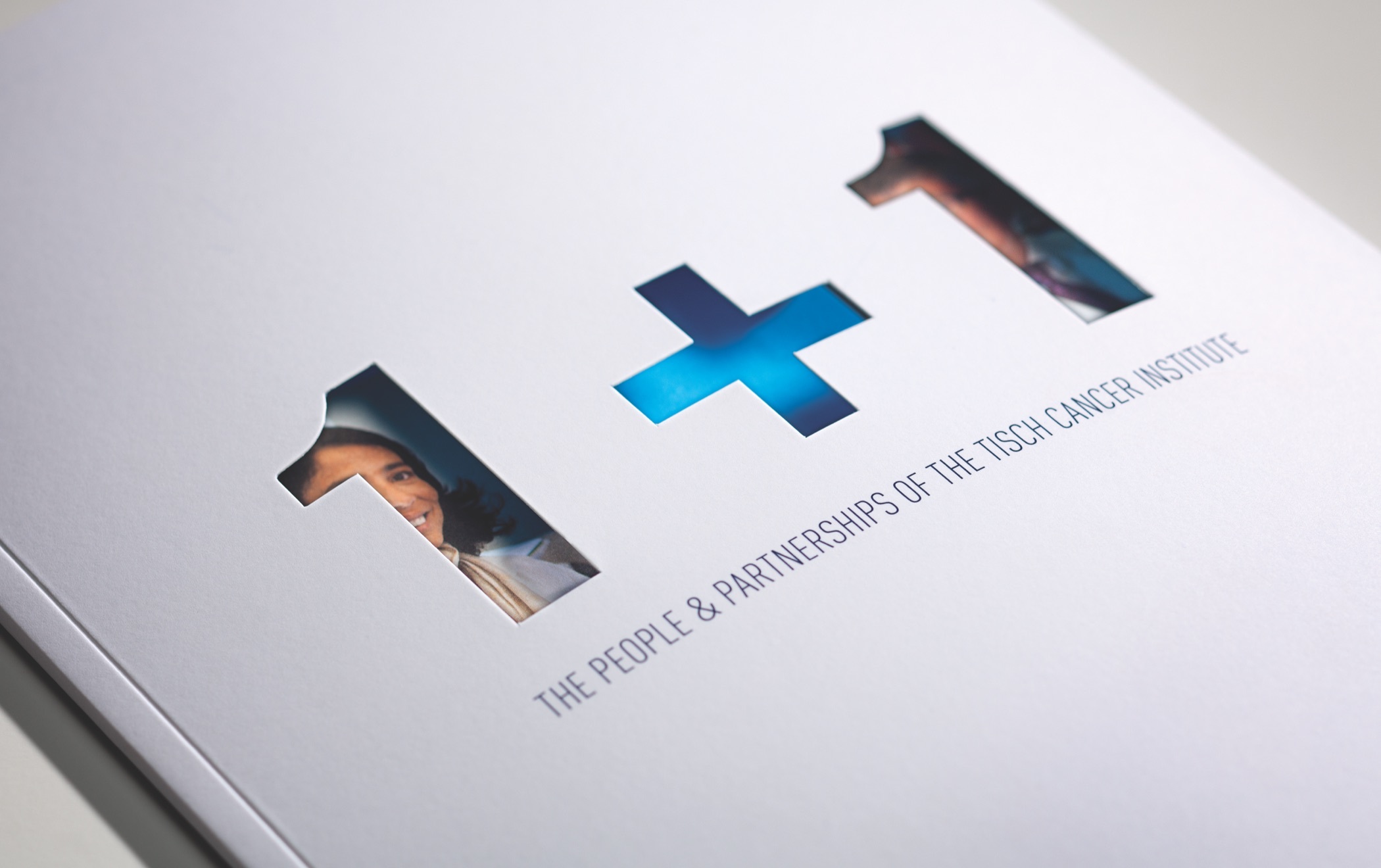 The title text one plus one die cut to reveal a photograph below on the cover of the Tisch Cancer Institute 2011 annual report.