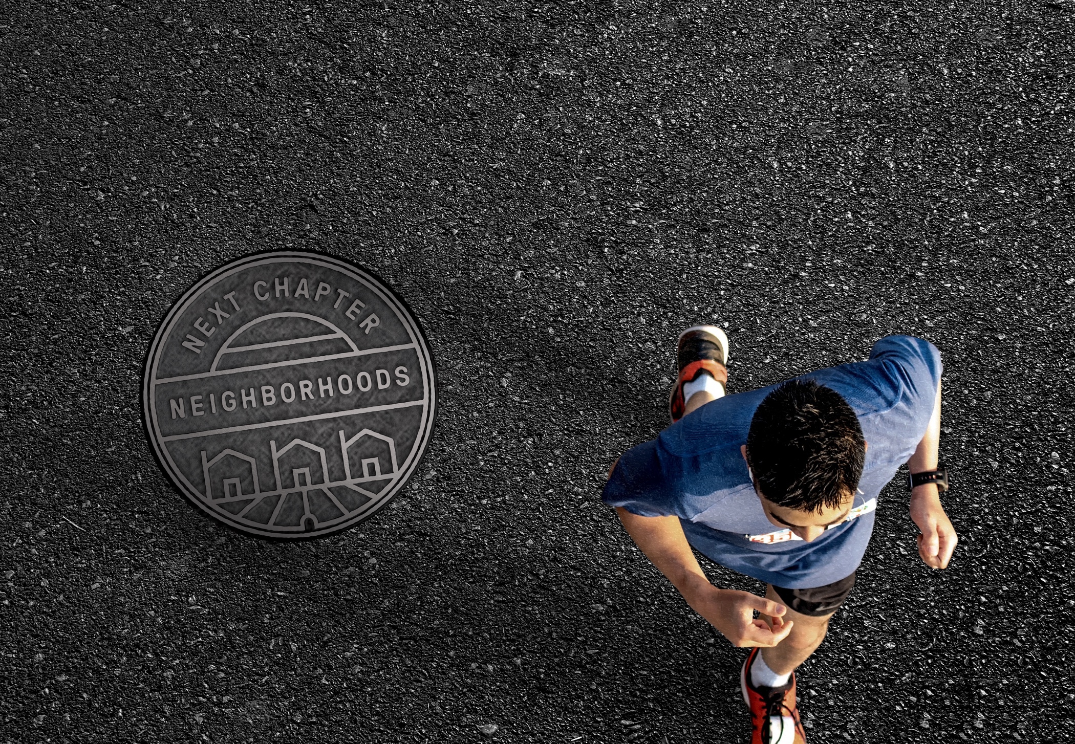 View from above as a jogger runs on a road past a Next Chapter branded manhole cover.