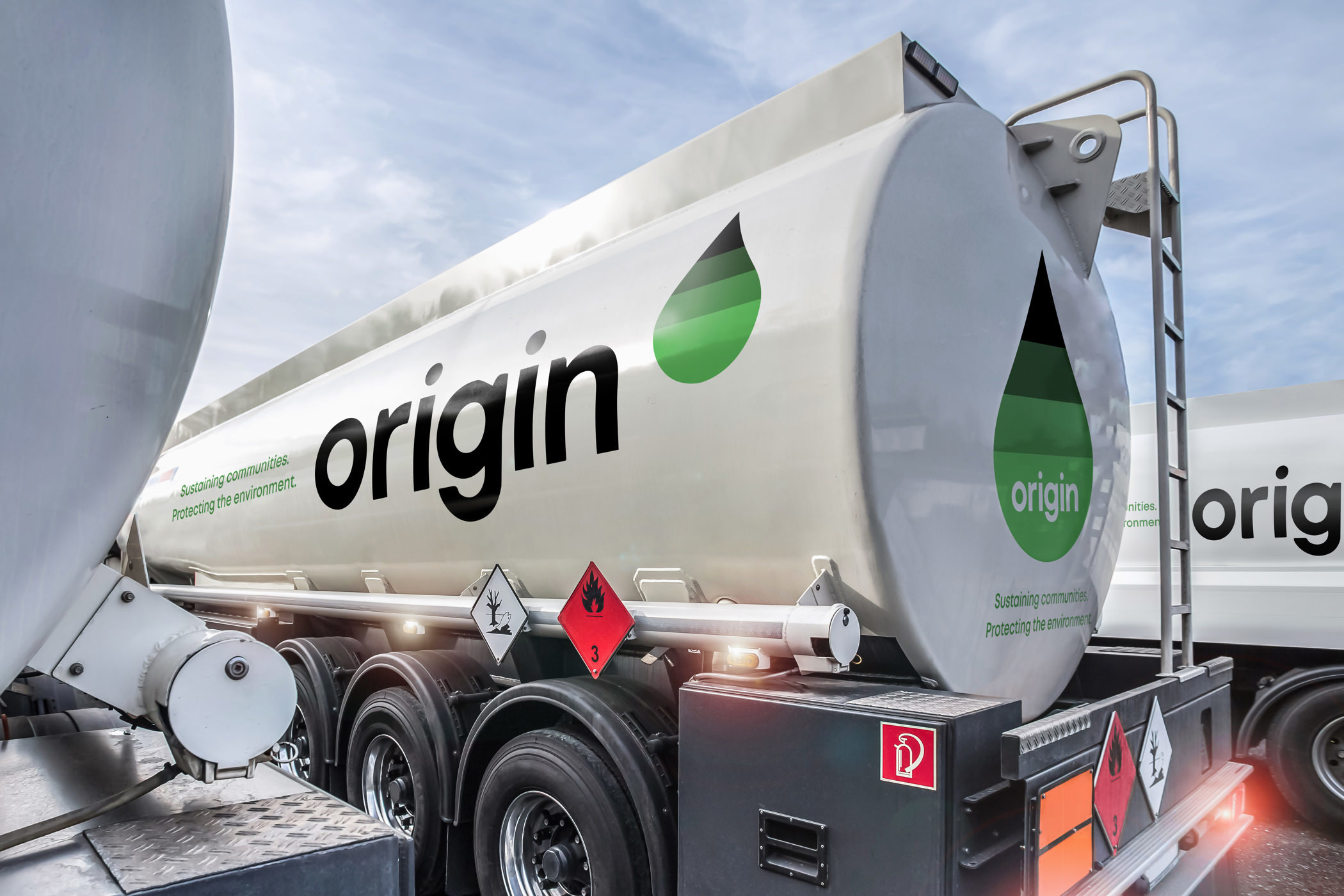 The Origin International logotype and green-gradient droplet symbol painted on a white tanker truck trailer.