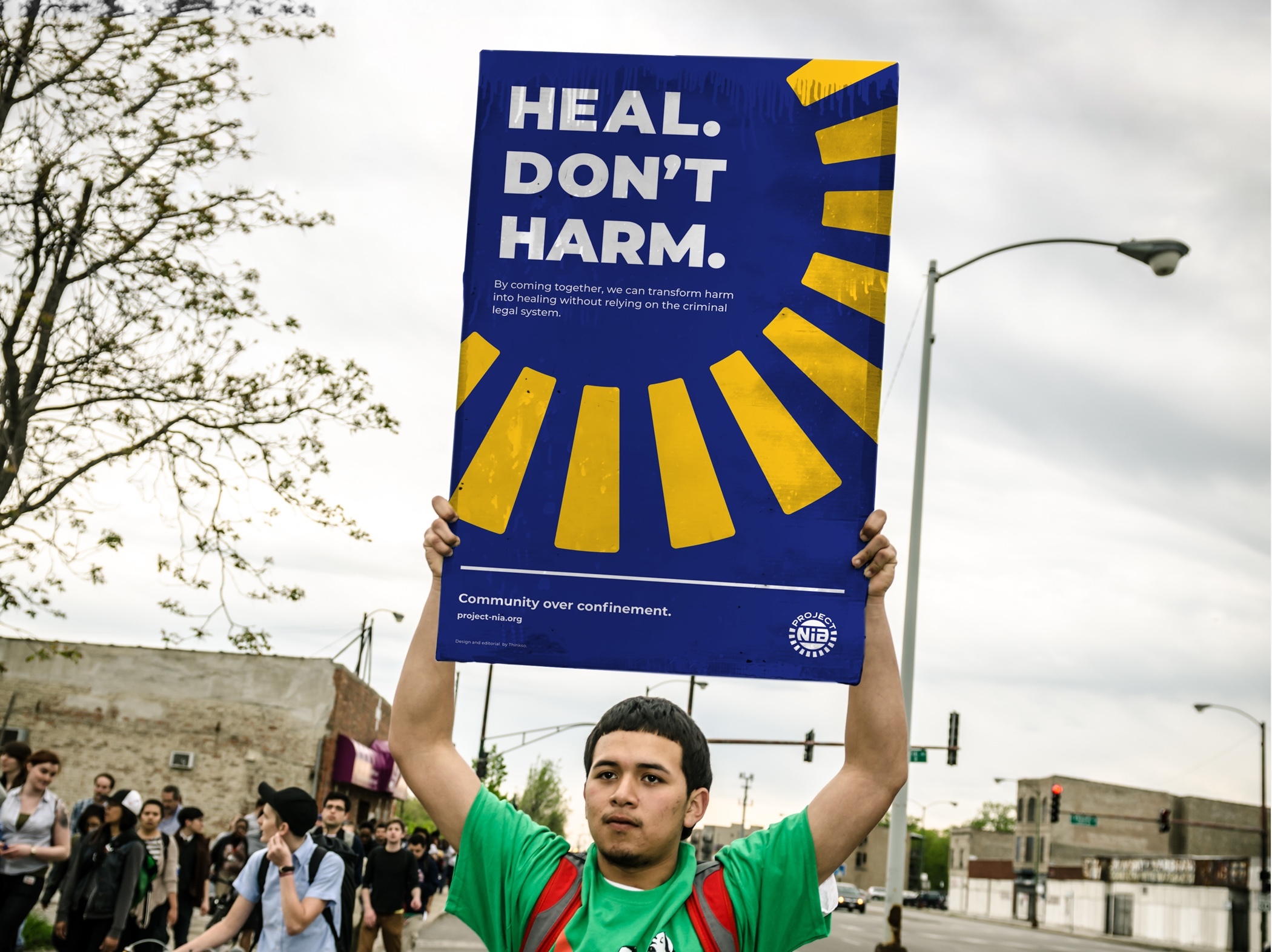 A young protester in a green shirt holding a Project Nia banner that read "Heal, don't harm" overhead.