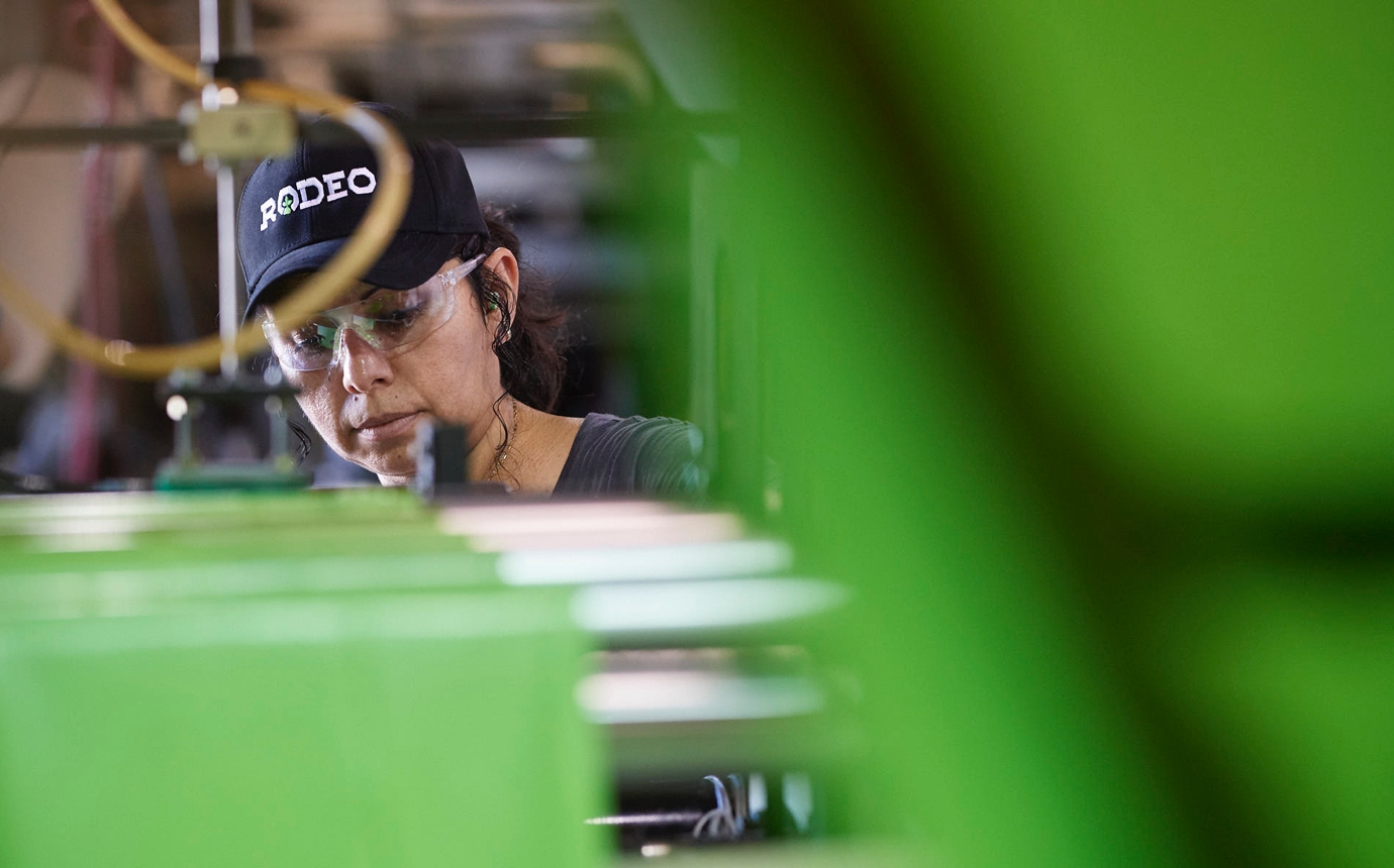 Rodeo Plastics worker in a company branded hat and saftety glasses works among the factory machinery.