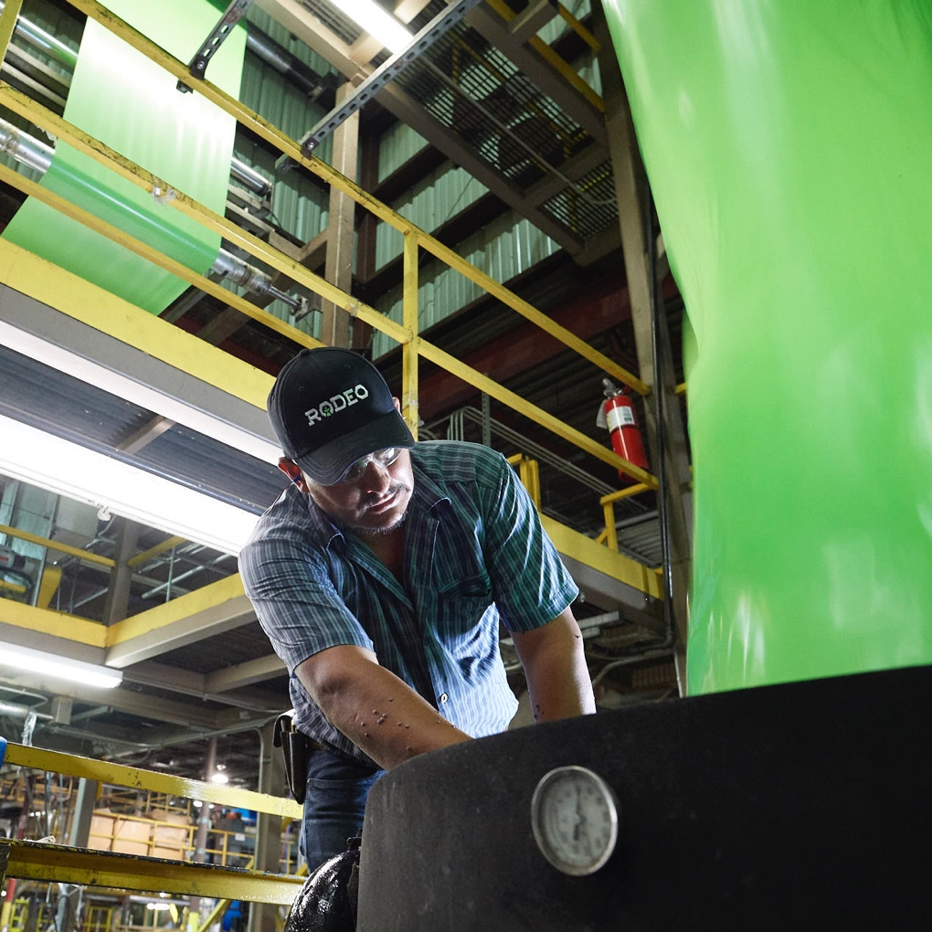A worker in a company branded hat bends over to operate machinery in the Rodeo Plastics factory.