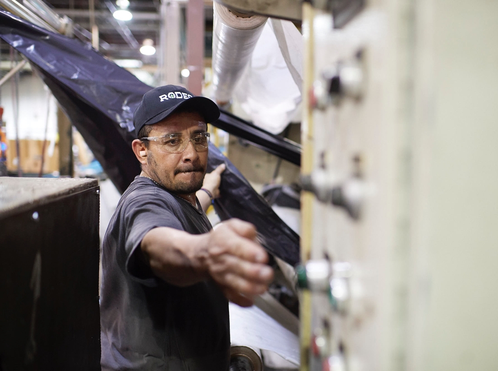 A worker in a Rodeo Plastics cap reaches out to flip a switch on machinery in the company's Mesquite Texas factory.