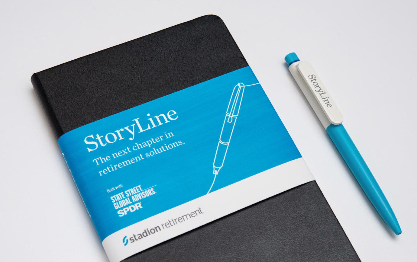 Notebook wrapped in Stadion StoryLine branding rests next to branded pen.