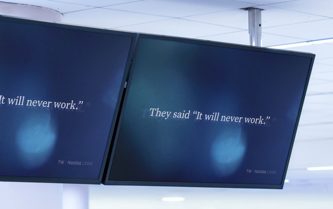 Overhead TV screens displaying an abstract video still frame with the words "They said it will never work."