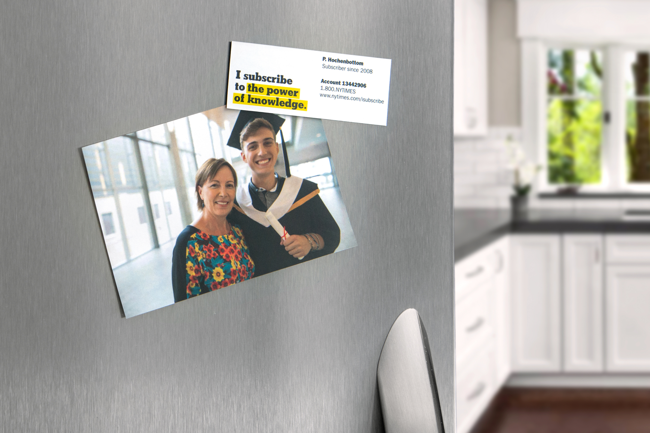 A New York Times promotional magnet that reads "I subscribe to the power of knowldege" holding a photo of graduate and his mom to a refrigerator.