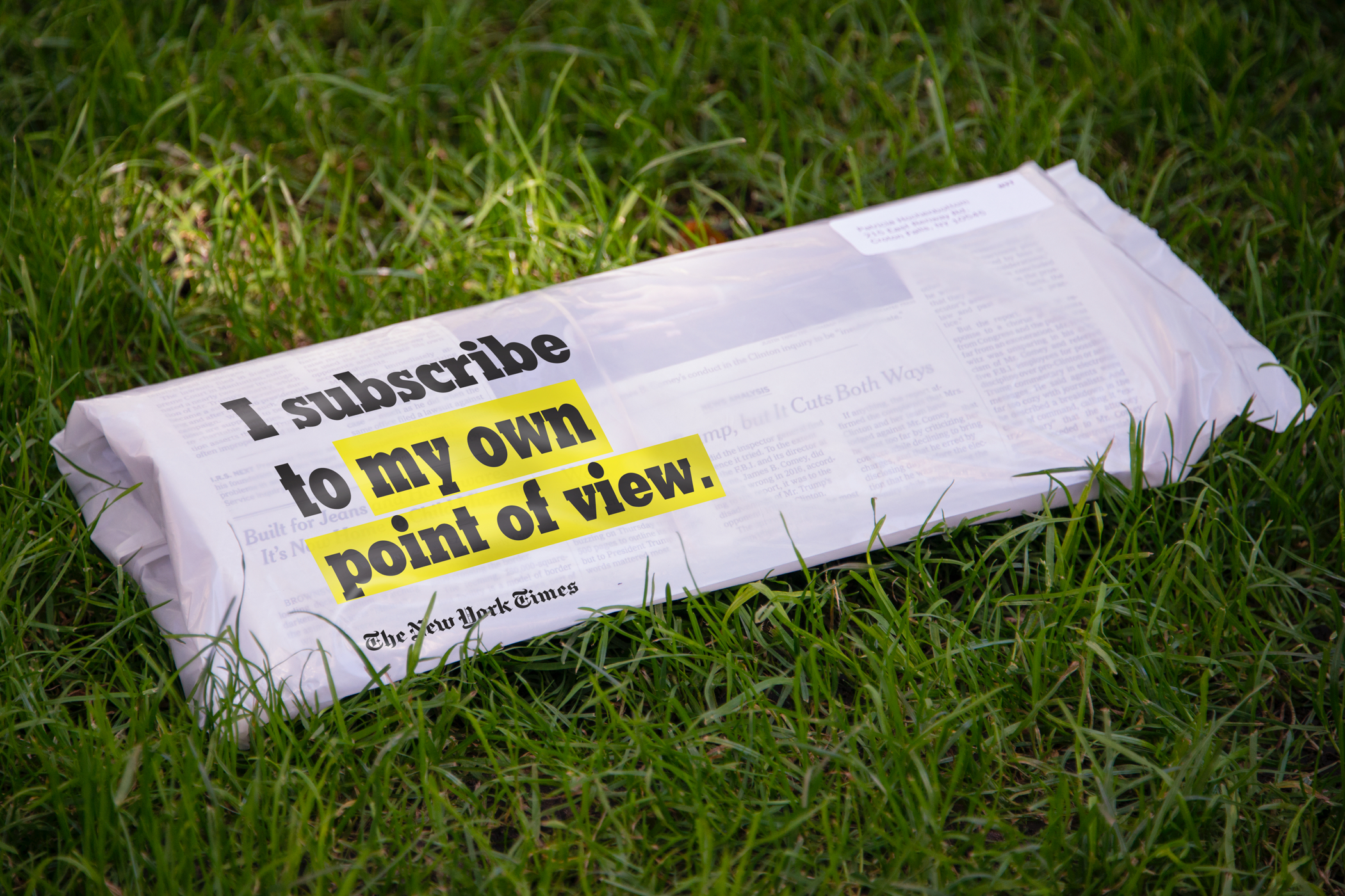 A New York TImes paper in plastic delivery bag printed with the text "I subscribe to my own point of view" on a grassy lawn.