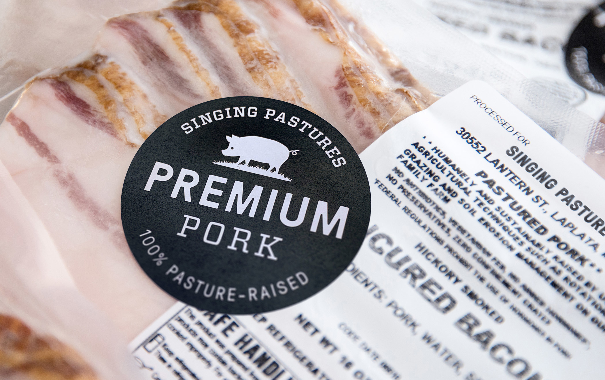 Close up a a Singing Pastures "Premium Pork" sticker affixed to a package of uncured, hickory smoked bacon.