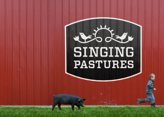 A large Singing Pastures logotype painted on a red barn wall with an illustration of a bird perched on a flowered vine.